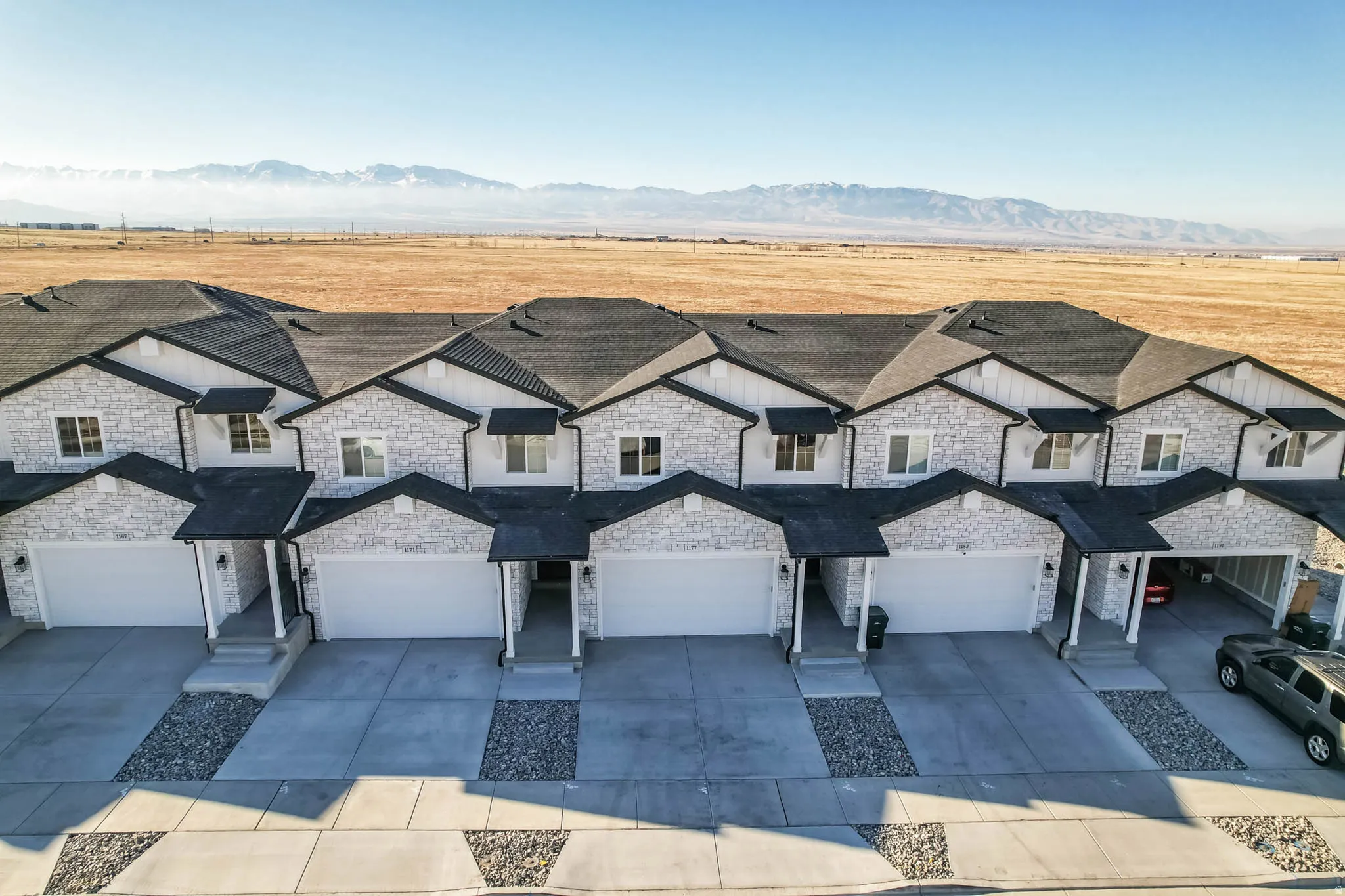 View of front of house with stone siding, a mountain view, concrete driveway, a garage, and roof with shingles