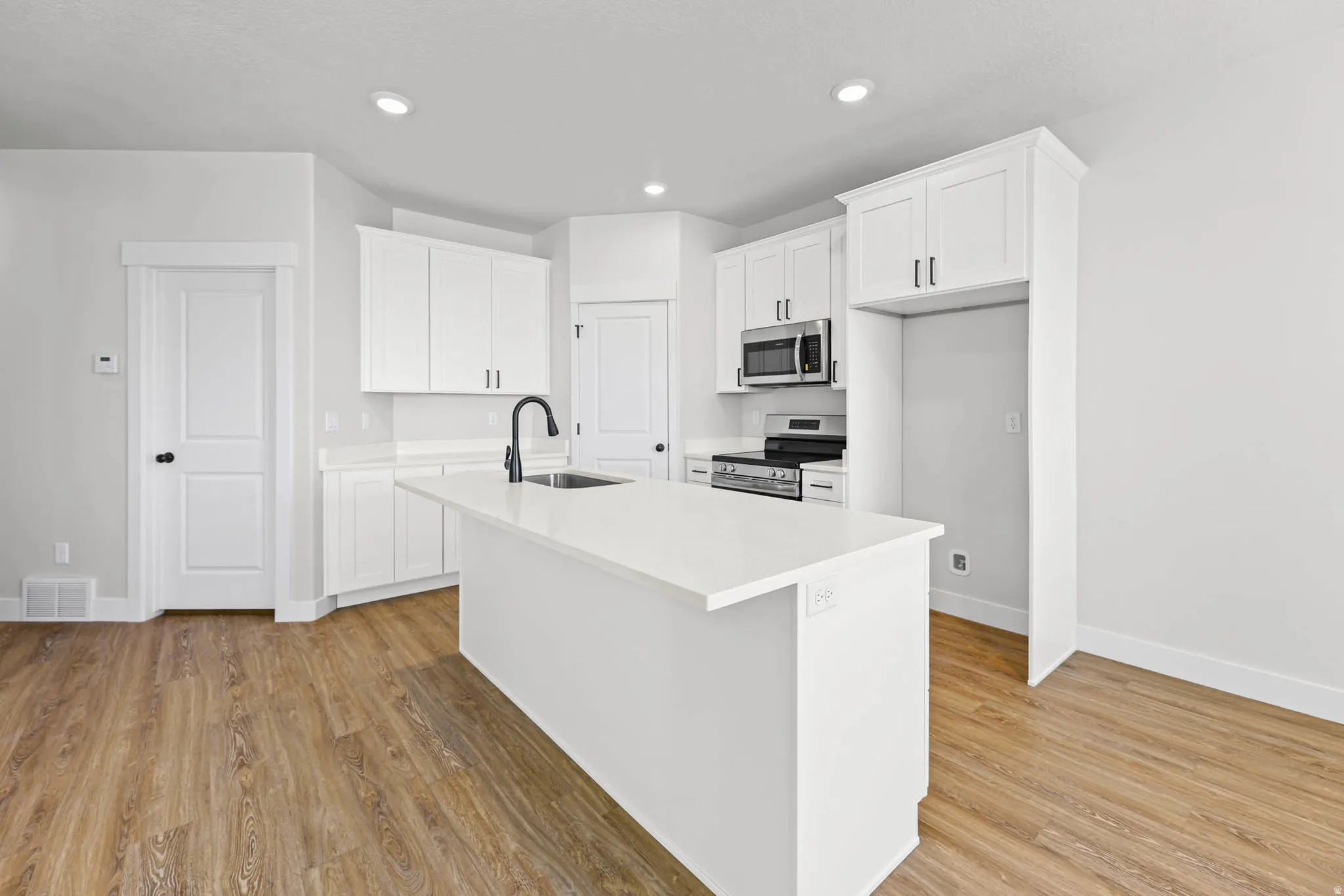 Kitchen featuring white cabinets, stainless steel appliances, an island with sink, light wood-type flooring, and recessed lighting