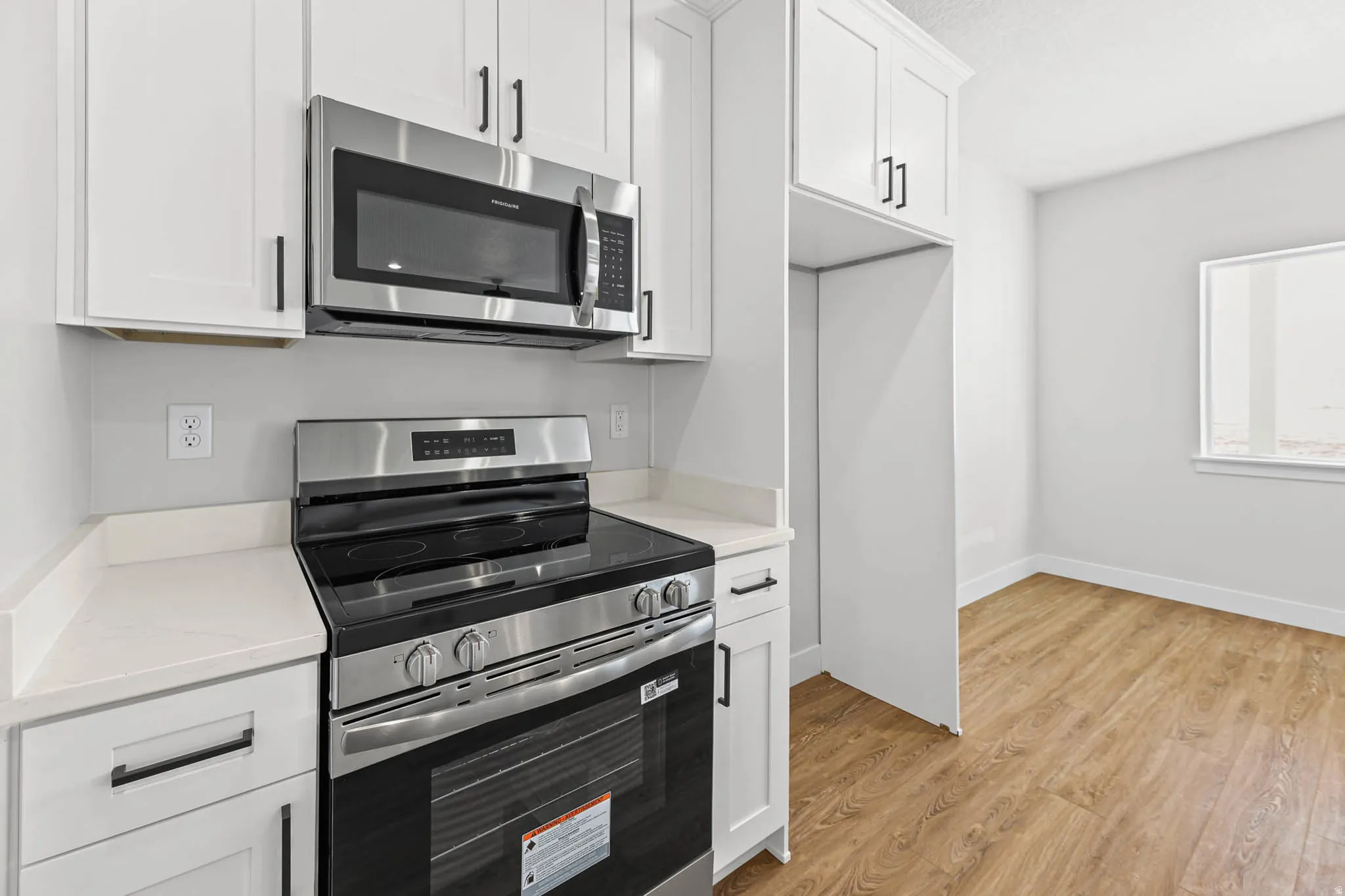 Kitchen with stainless steel appliances, white cabinetry, light wood finished floors, and light stone countertops
