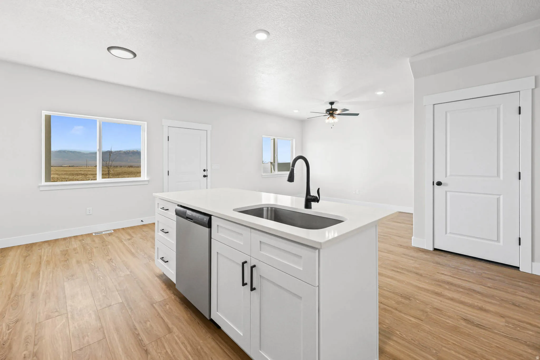 Kitchen featuring an island with sink, light wood finished floors, white cabinets, light stone countertops, and ceiling fan