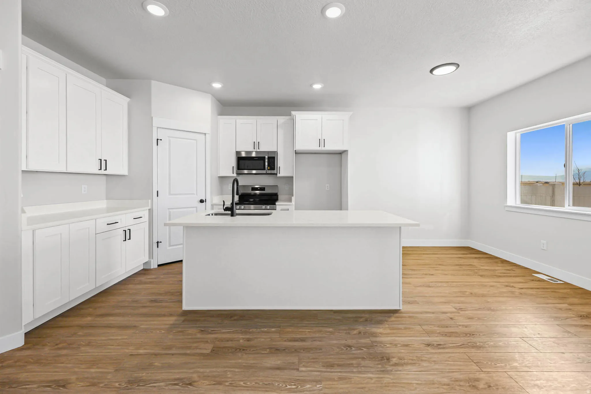 Kitchen featuring white cabinetry, dark wood-style floors, stainless steel appliances, a center island with sink, and recessed lighting
