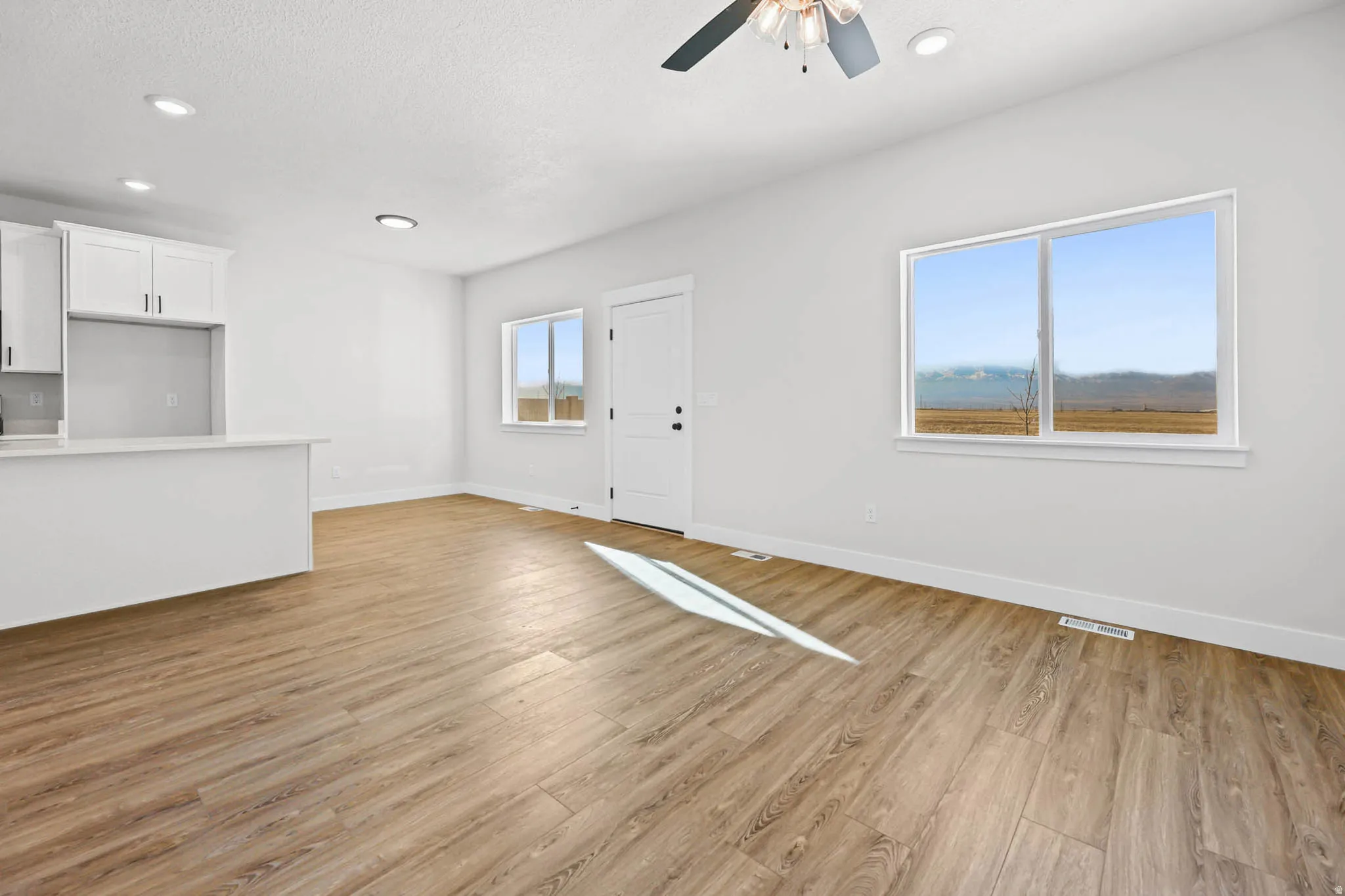 Unfurnished living room featuring light wood-style flooring, ceiling fan, a textured ceiling, and recessed lighting