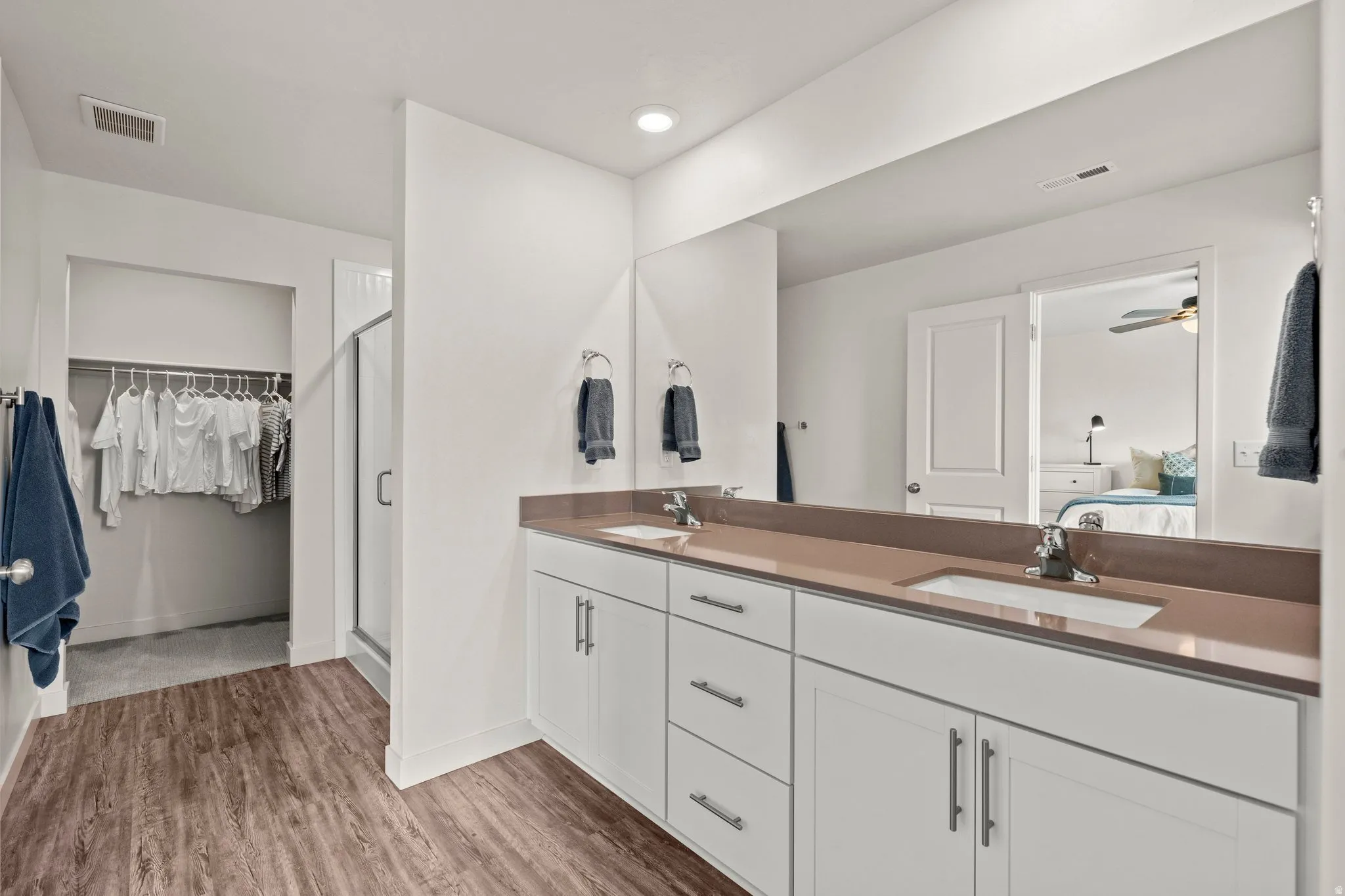 Full bath featuring double vanity, a spacious closet, dark wood-style flooring, a stall shower, and ensuite bath
