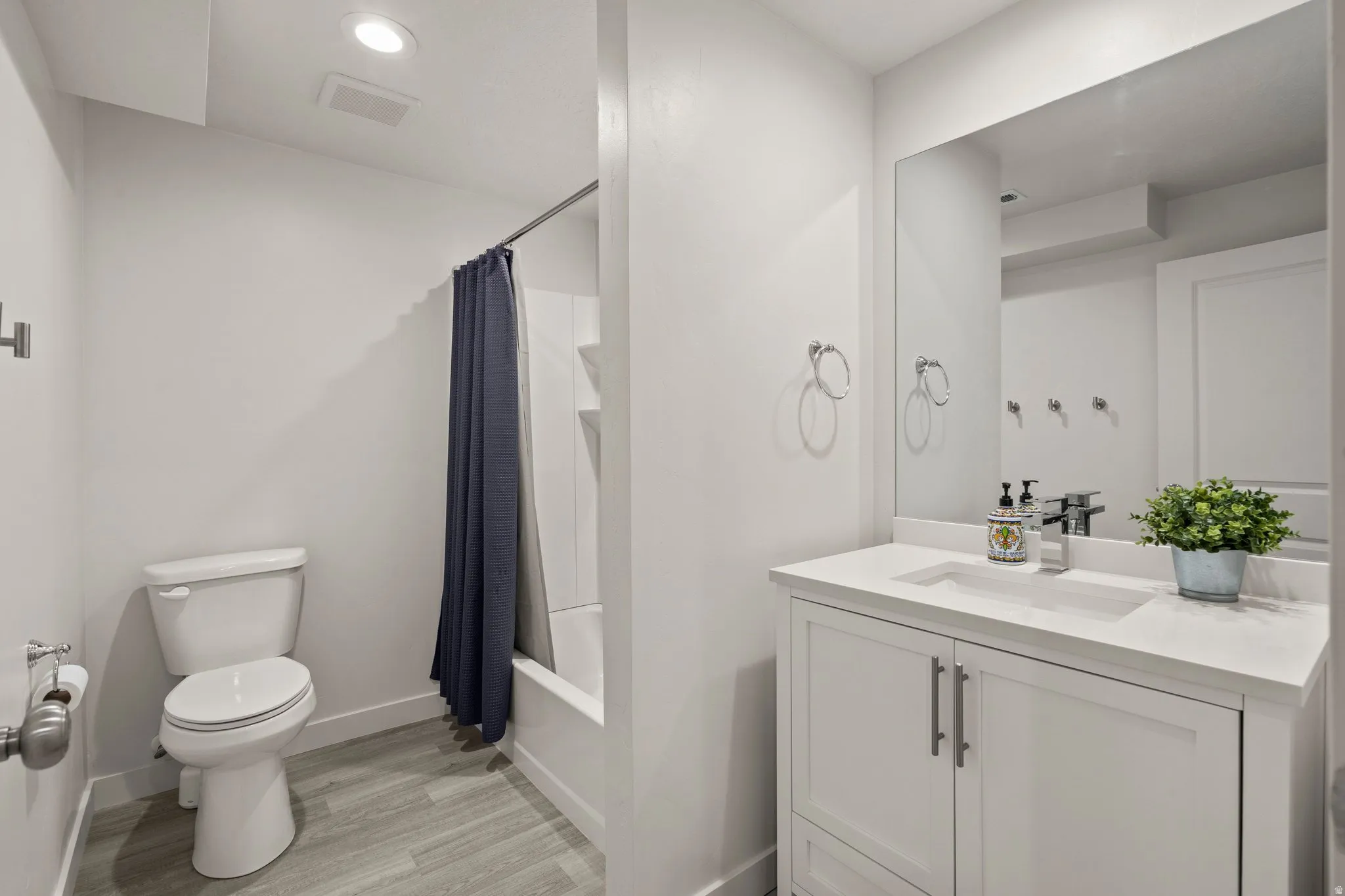 Bathroom featuring vanity, light wood finished floors, shower / tub combo with curtain, and recessed lighting
