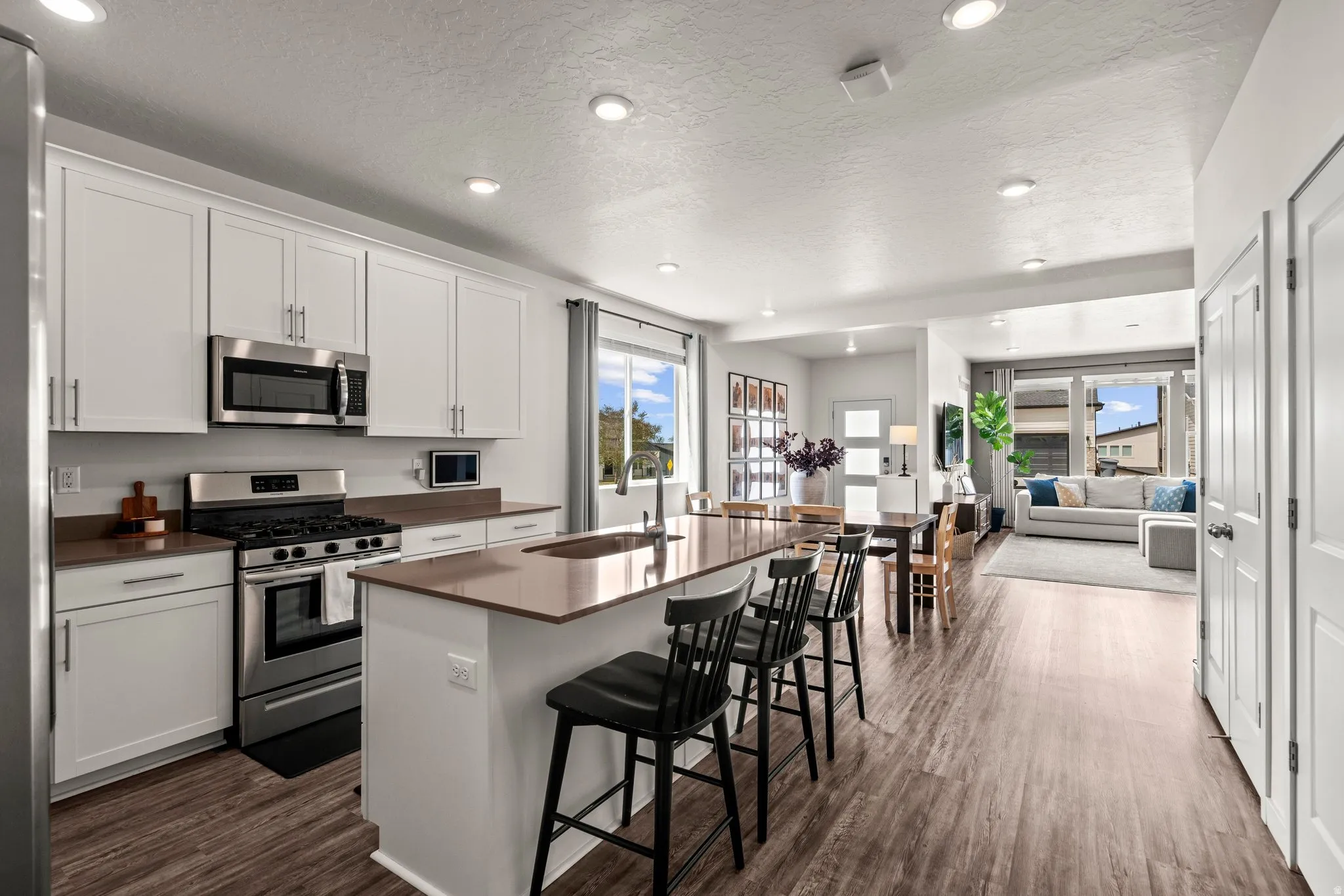 Kitchen with stainless steel appliances, white cabinetry, a center island with sink, a kitchen bar, and recessed lighting
