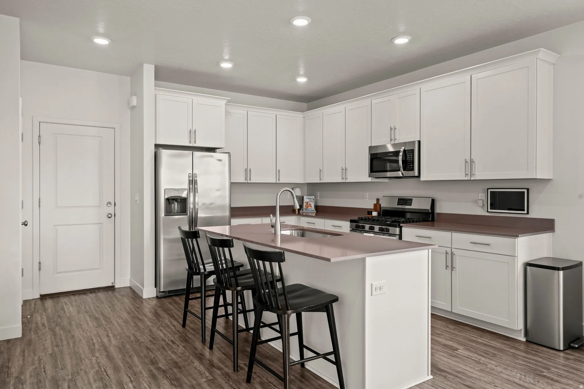 Kitchen featuring white cabinetry, stainless steel appliances, a kitchen breakfast bar, an island with sink, and dark wood-style flooring