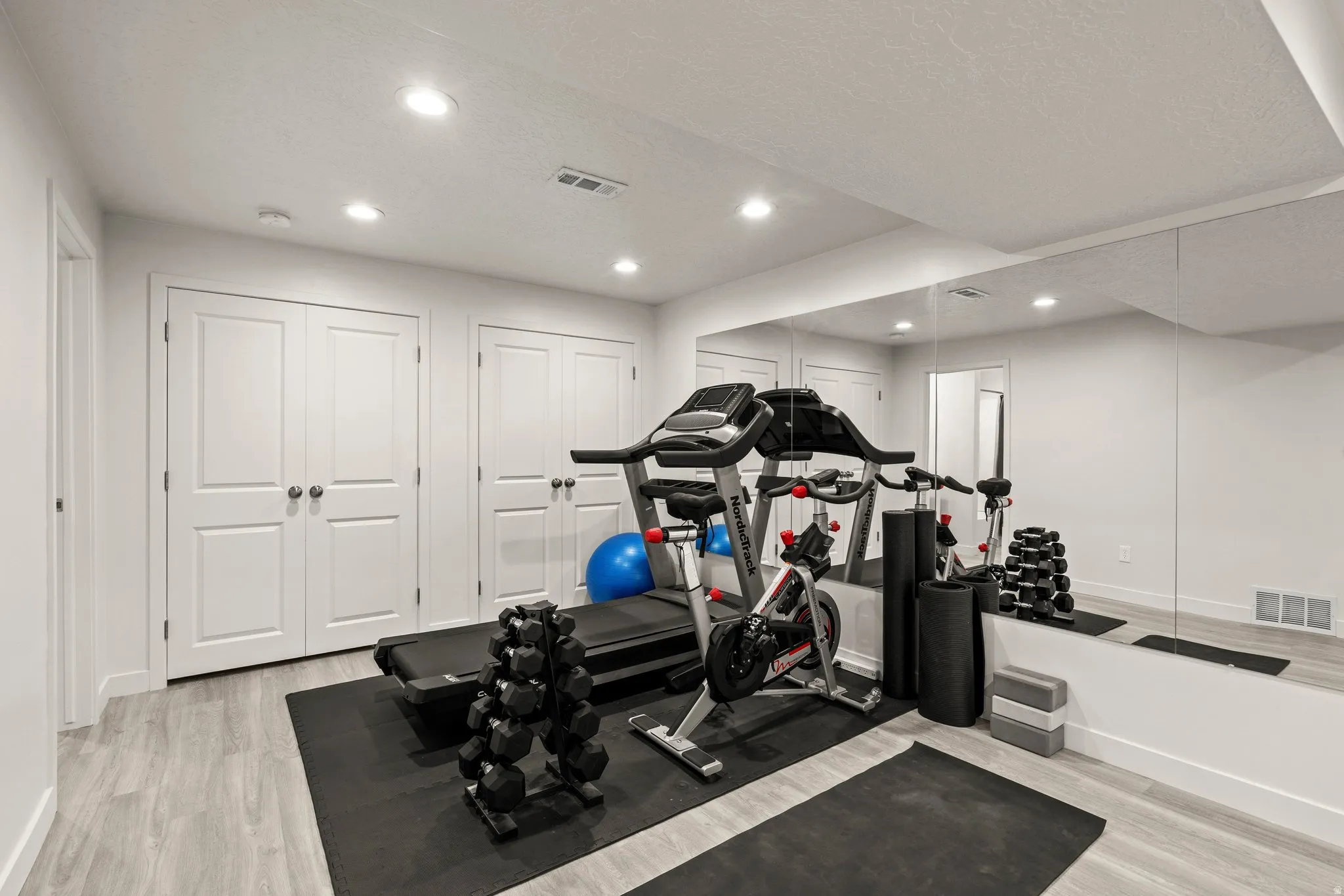 Exercise area with light wood-type flooring, recessed lighting, and a textured ceiling