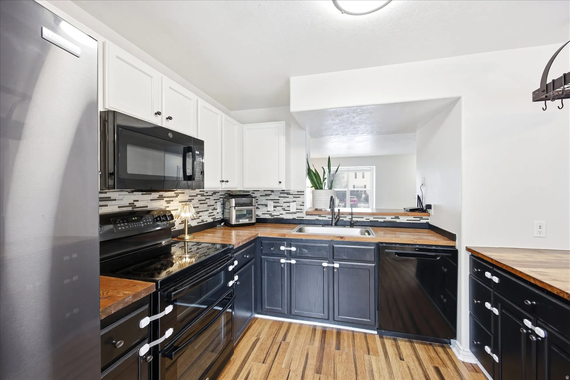 Dual tone kitchen with black appliances, two tone cabinets, butcher block countertops, light wood finished floors, and backsplash