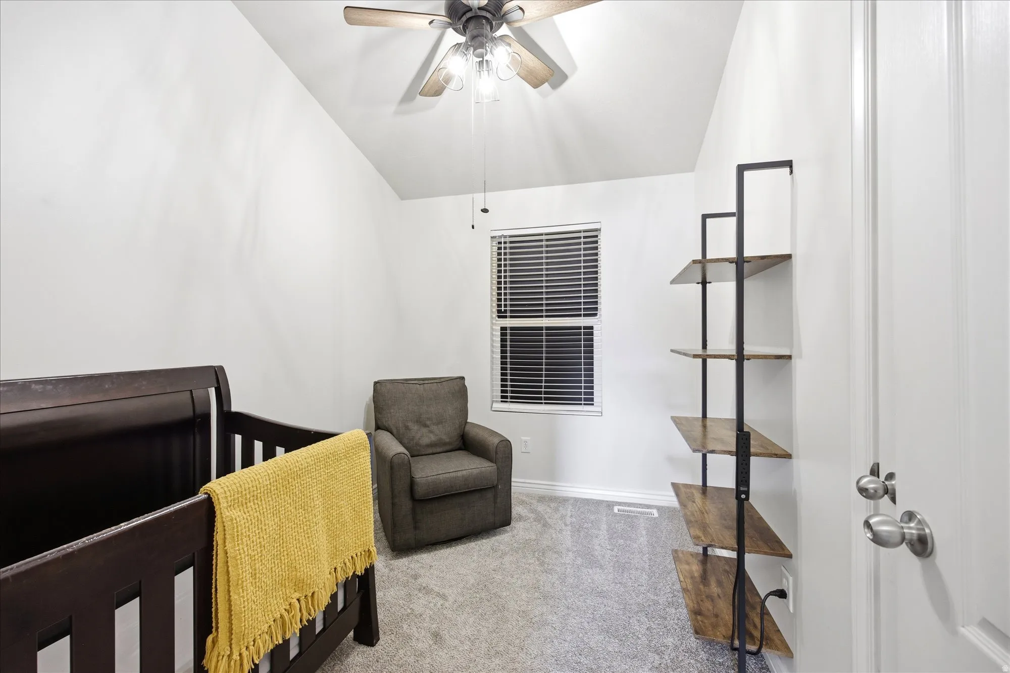 Carpeted bedroom featuring vaulted ceiling, a crib, and a ceiling fan