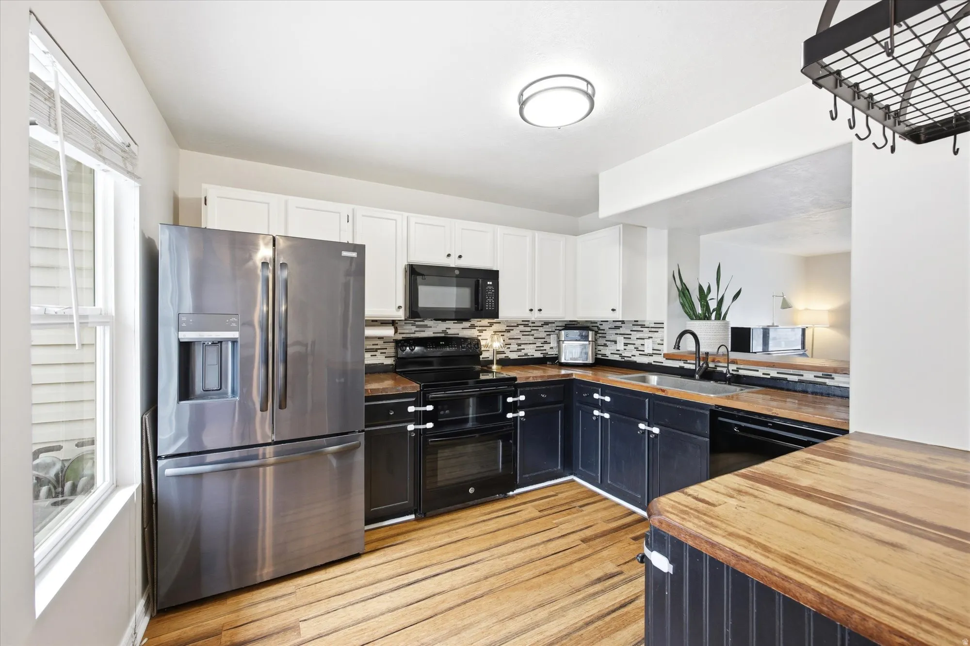 Kitchen with black appliances, two tone cabinetry, wood counters, light wood-style flooring, and backsplash
