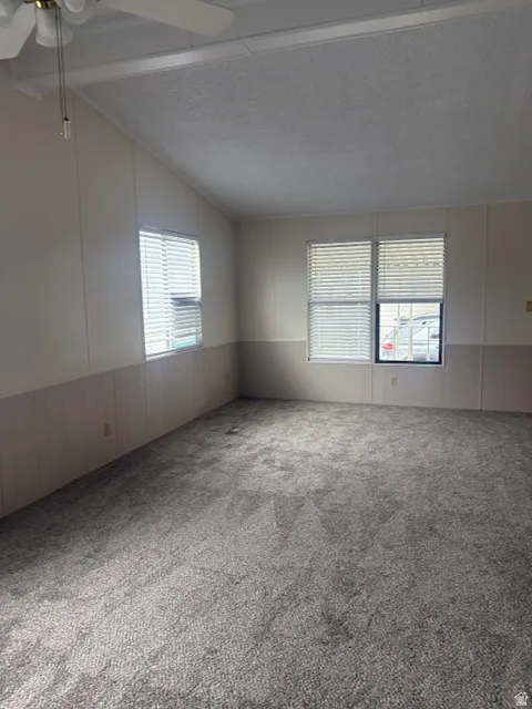 Carpeted empty room with ceiling fan, a decorative wall, wainscoting, and plenty of natural light