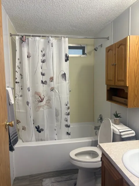 Full bath with vanity, shower / bath combo, and a textured ceiling