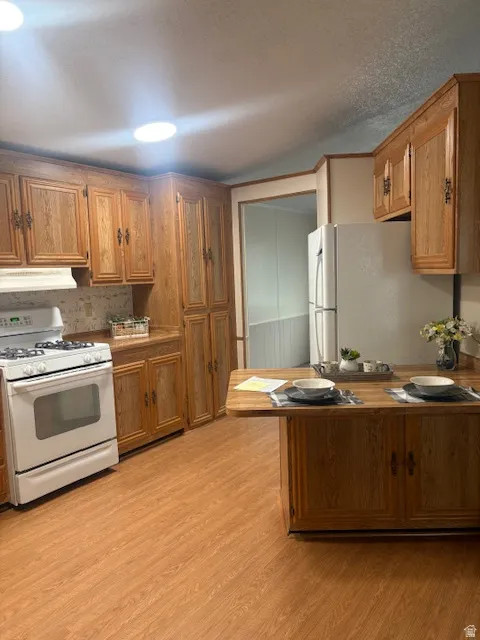 Kitchen featuring wood finish cabinetry, white appliances, light wood-style floors, a peninsula, and a textured ceiling