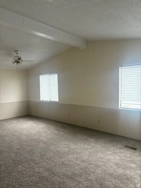 Carpeted empty room with beamed ceiling, a textured ceiling, a ceiling fan, a wainscoted wall, and a decorative wall