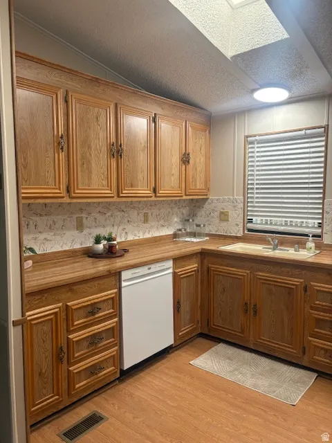 Kitchen featuring wood finish cabinetry, dishwasher, a textured ceiling, and light wood-style flooring