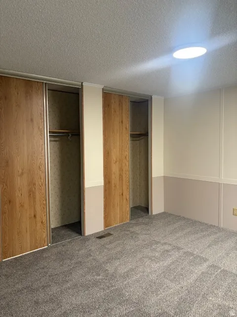 Unfurnished bedroom with a textured ceiling, multiple closets, and carpet floors