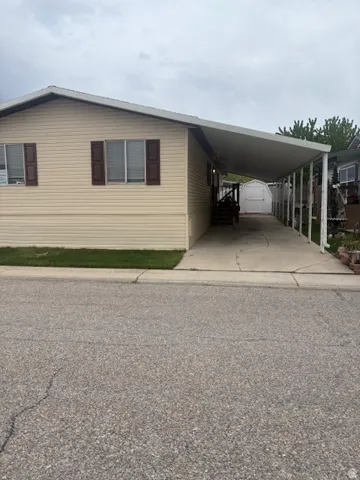 View of front of house featuring driveway, a carport, and a storage unit
