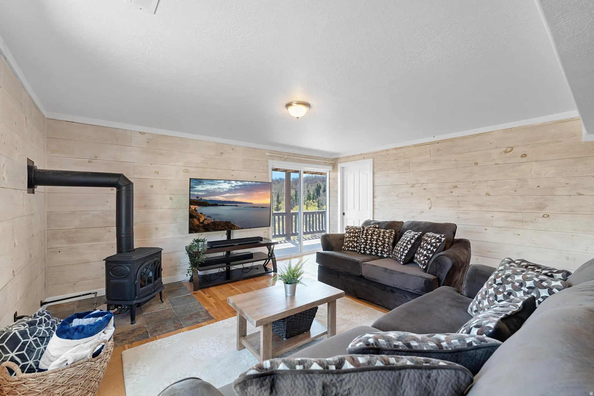 Living area featuring a cast iron wood-burning stove on a stone tile hearth, wood-finish flooring, plank wall finishes, and a sliding glass door opening to a balcony with mountain scenery