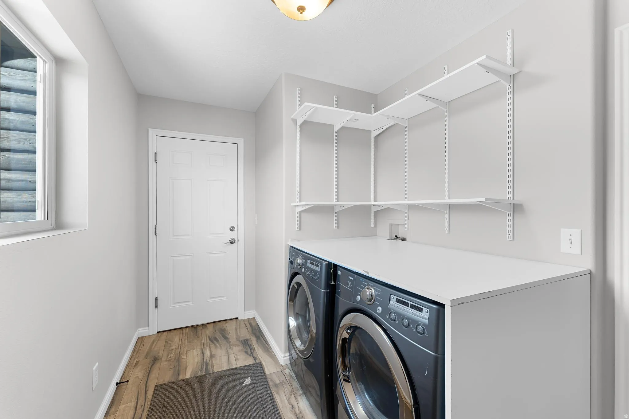 Dedicated laundry space featuring side-by-side appliances, a white laminate countertop, and wood-finish flooring