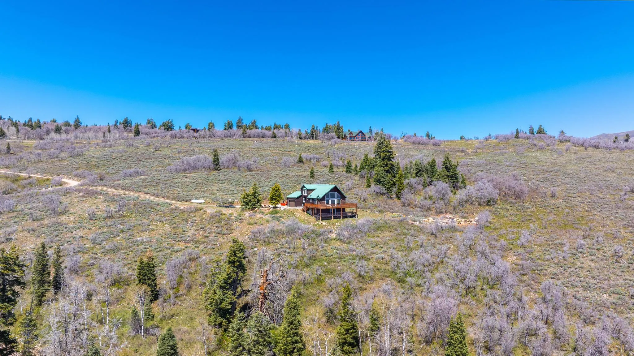 Spacious hillside property featuring a multi-level residence with a wood-finish exterior, a dark green roof, and a large wraparound deck