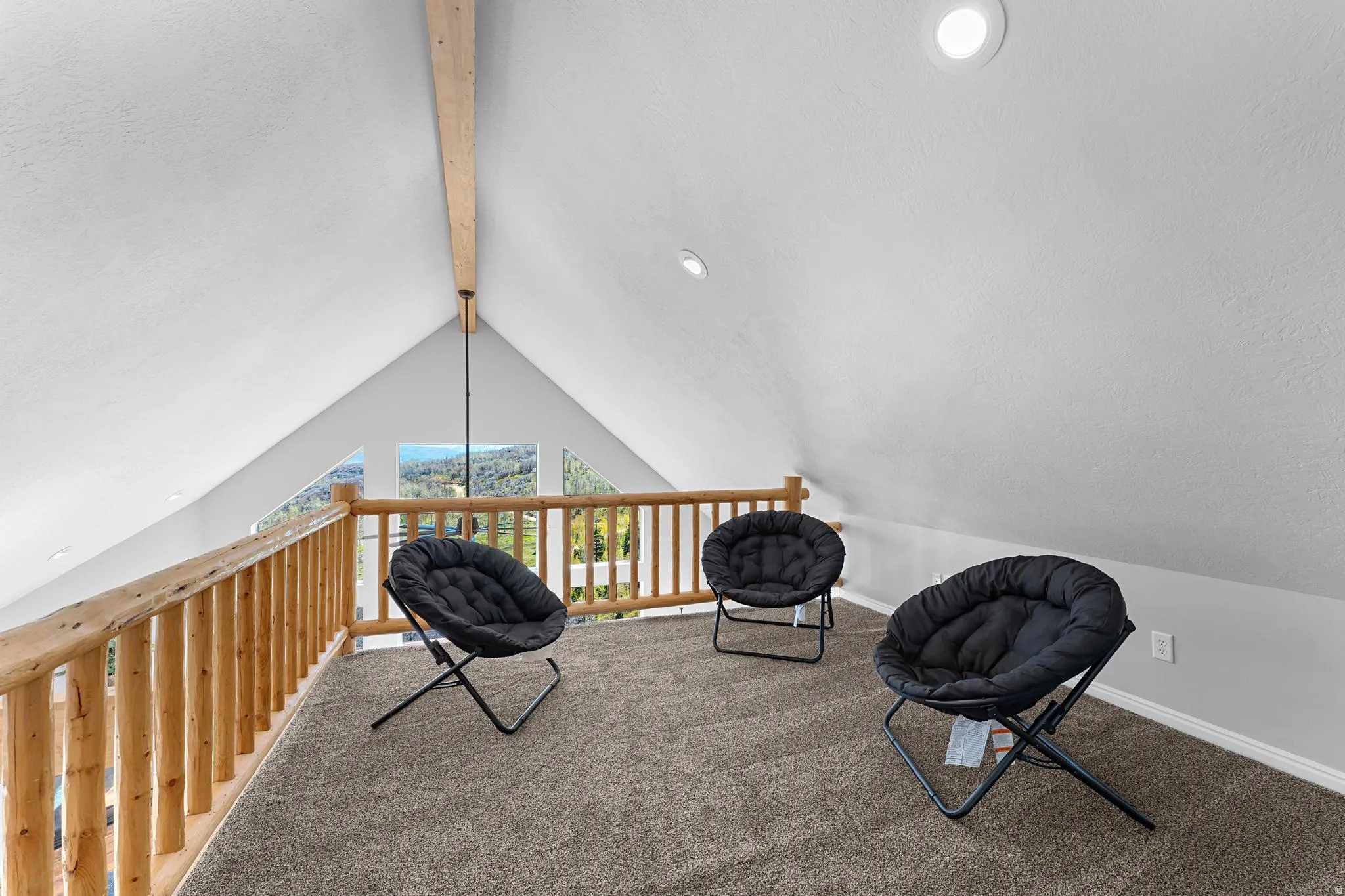 Loft area featuring a vaulted ceiling with exposed wood beam, recessed lighting, and a wood railing overlooking the surrounding scenery