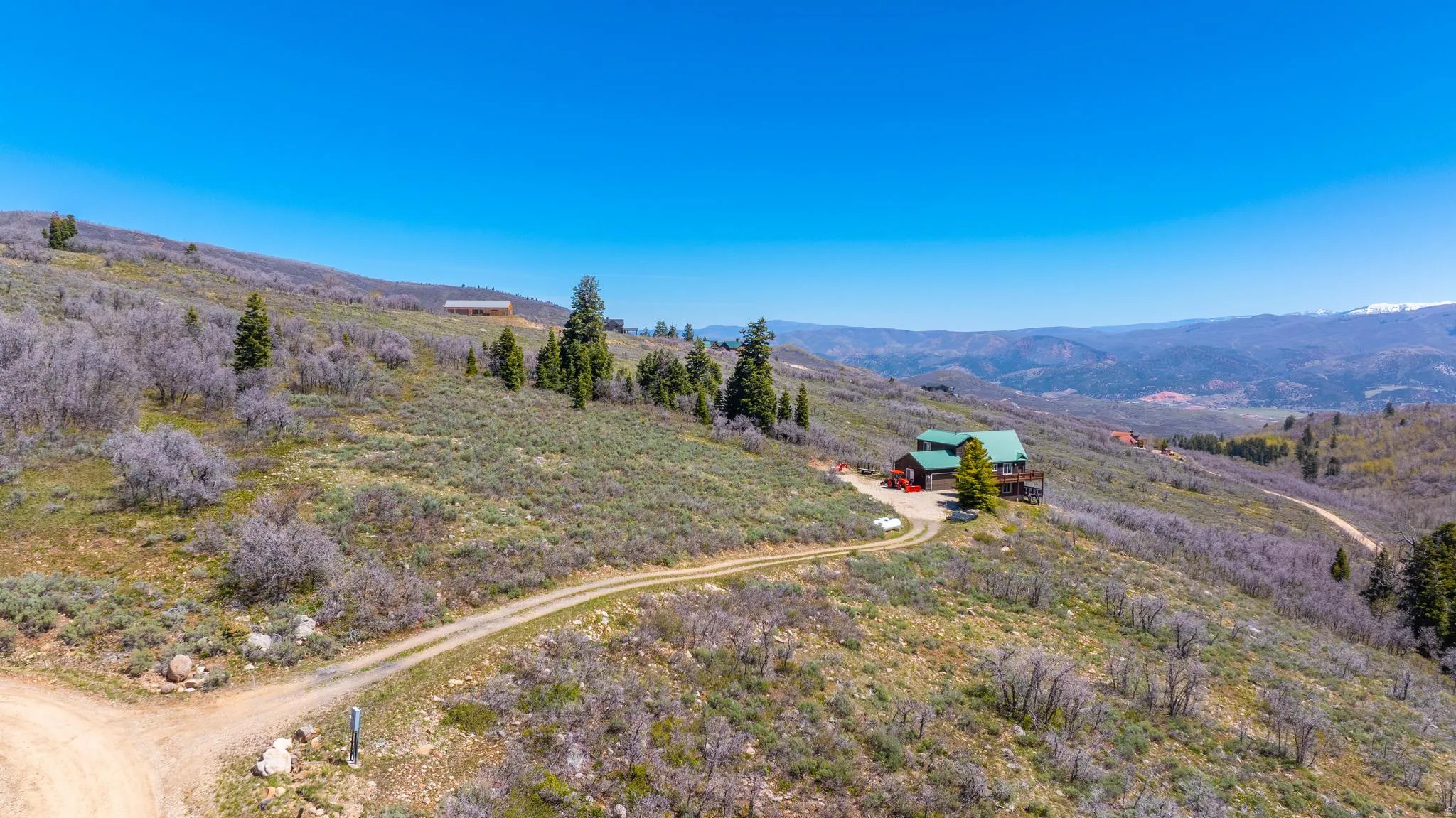 Hillside residence with a green roof, multiple outdoor decks, and a detached garage, set against a mountainous backdrop