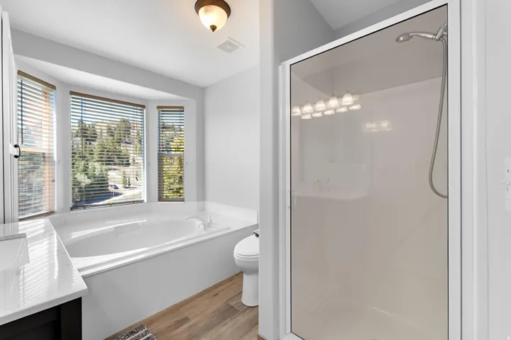 Soaking tub with a bay window, separate glass-enclosed shower, wood-finish flooring, and a vanity with a white countertop