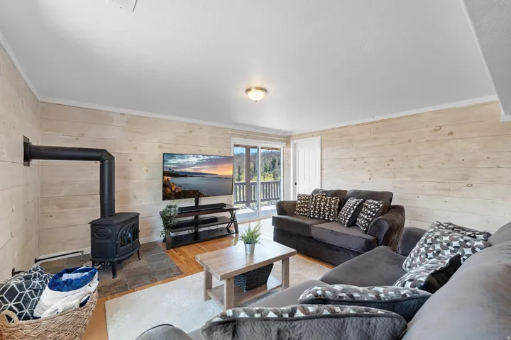 Living area featuring a cast iron wood-burning stove on a stone tile hearth, wood-finish flooring, plank wall finishes, and a sliding glass door opening to a balcony with mountain scenery