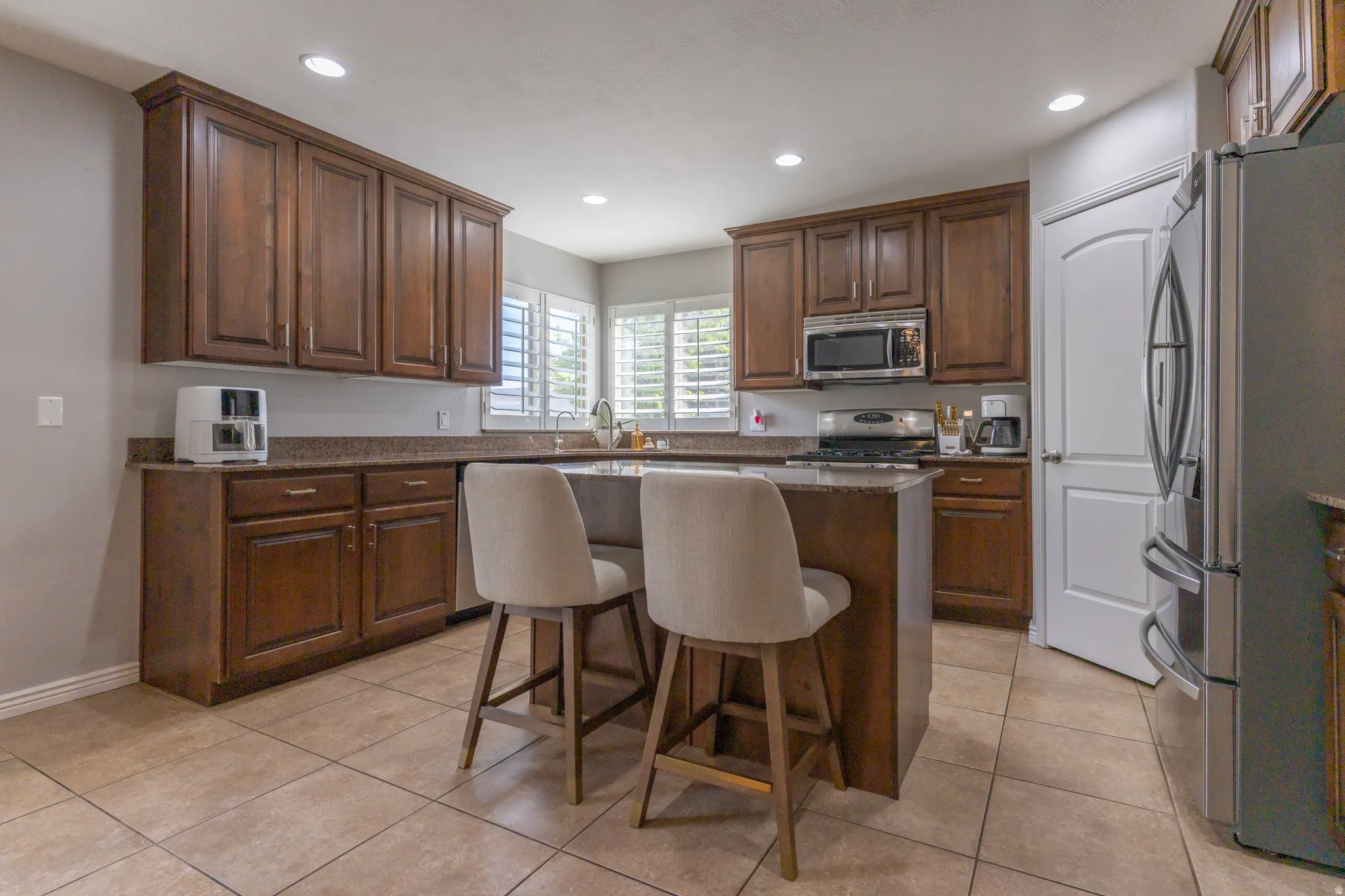 Kitchen featuring stainless steel appliances, a kitchen bar, light tile patterned floors, a center island, and dark stone counters