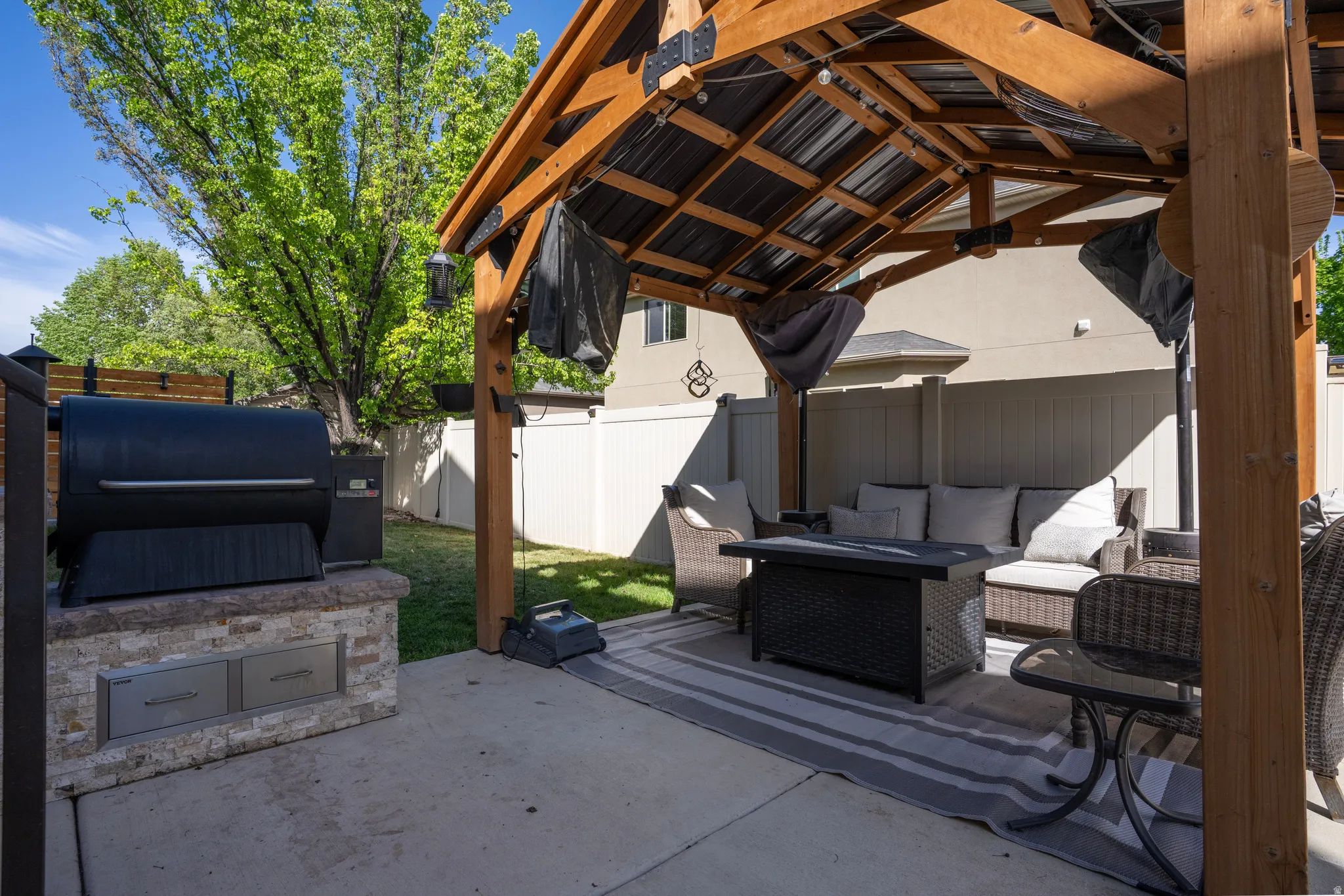 Fenced backyard with a gazebo, a patio area, a fire pit, and an outdoor kitchen and area to lounge
