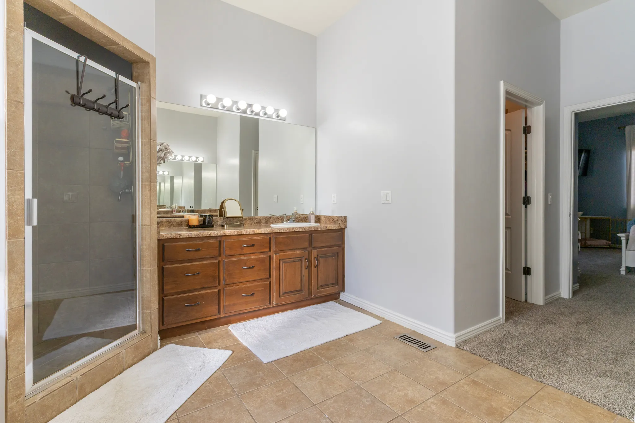 Full bath with vanity, light carpet, a shower stall, and light tile patterned flooring