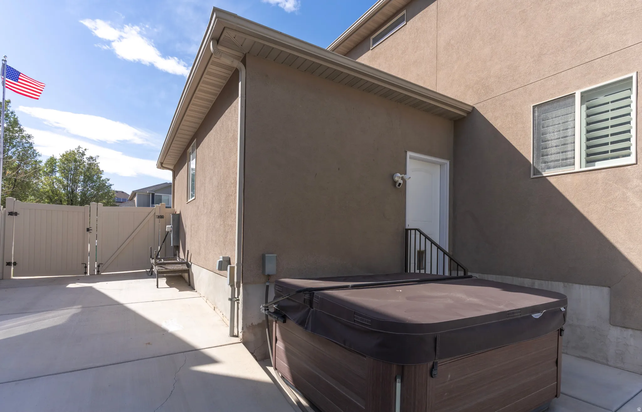 Back of property featuring a gate, stucco siding, and a hot tub