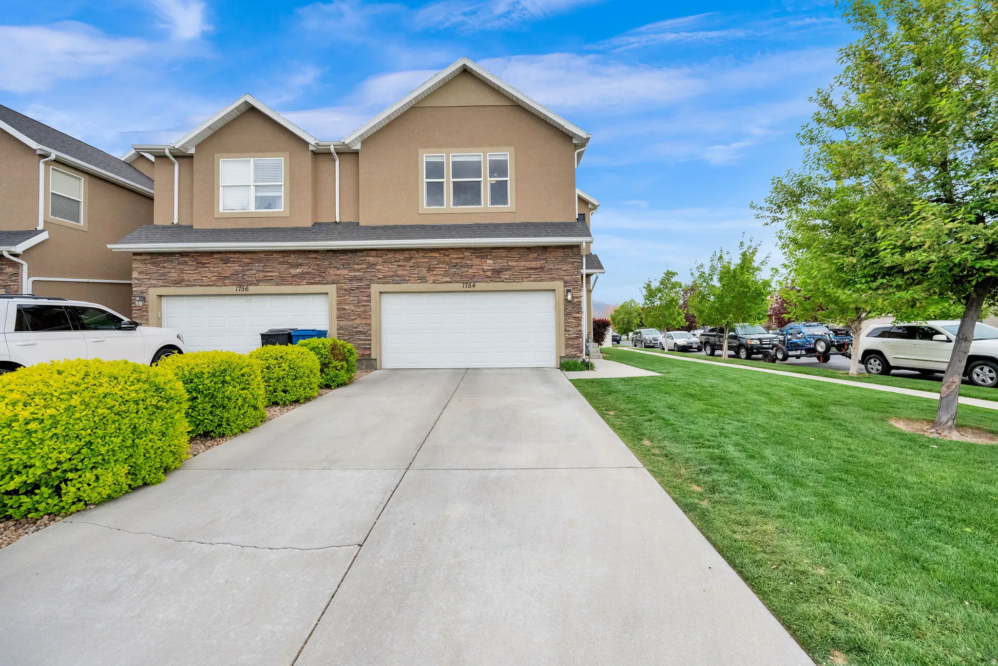 View of front facade featuring concrete driveway, a garage, stone siding, stucco siding, and a front lawn