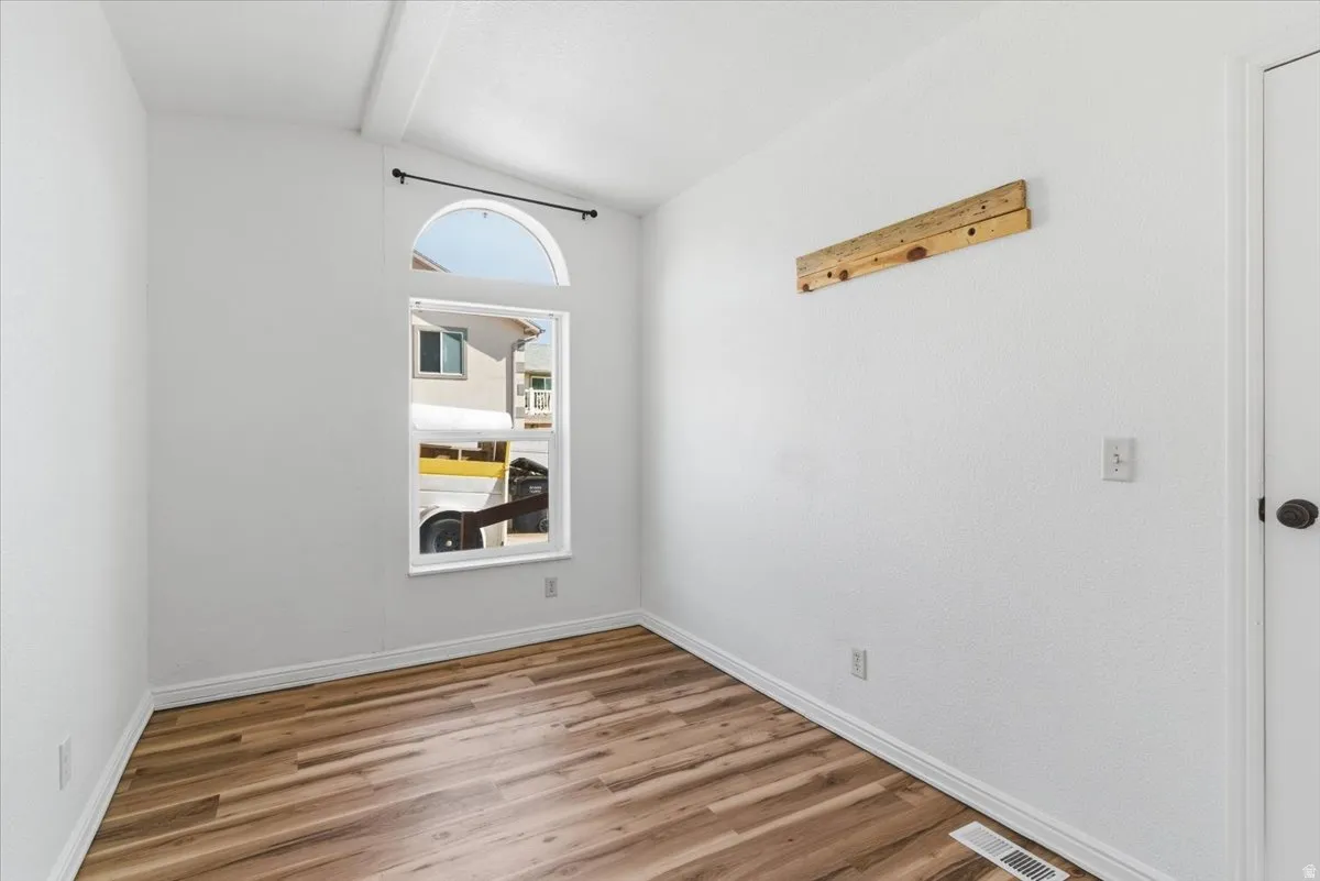 Spare room with light wood-style flooring and vaulted ceiling with beams