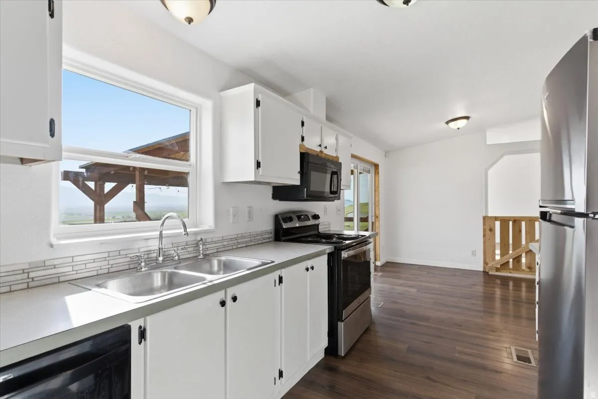 Kitchen with stainless steel appliances, light countertops, white cabinetry, and dark wood-style flooring