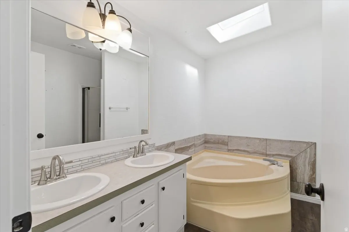 Full bath with a skylight, double vanity, a garden tub, decorative backsplash, and an enclosed shower