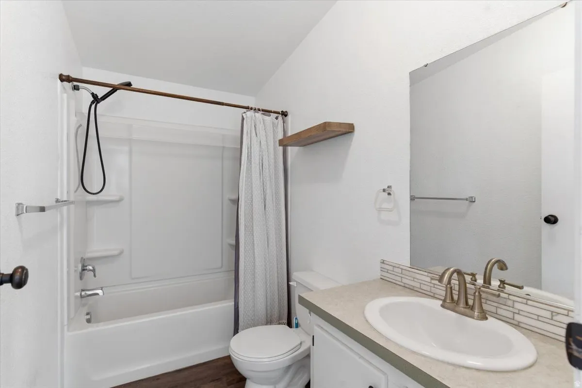 Full bath featuring vanity, shower / bathtub combination with curtain, and dark wood finished floors