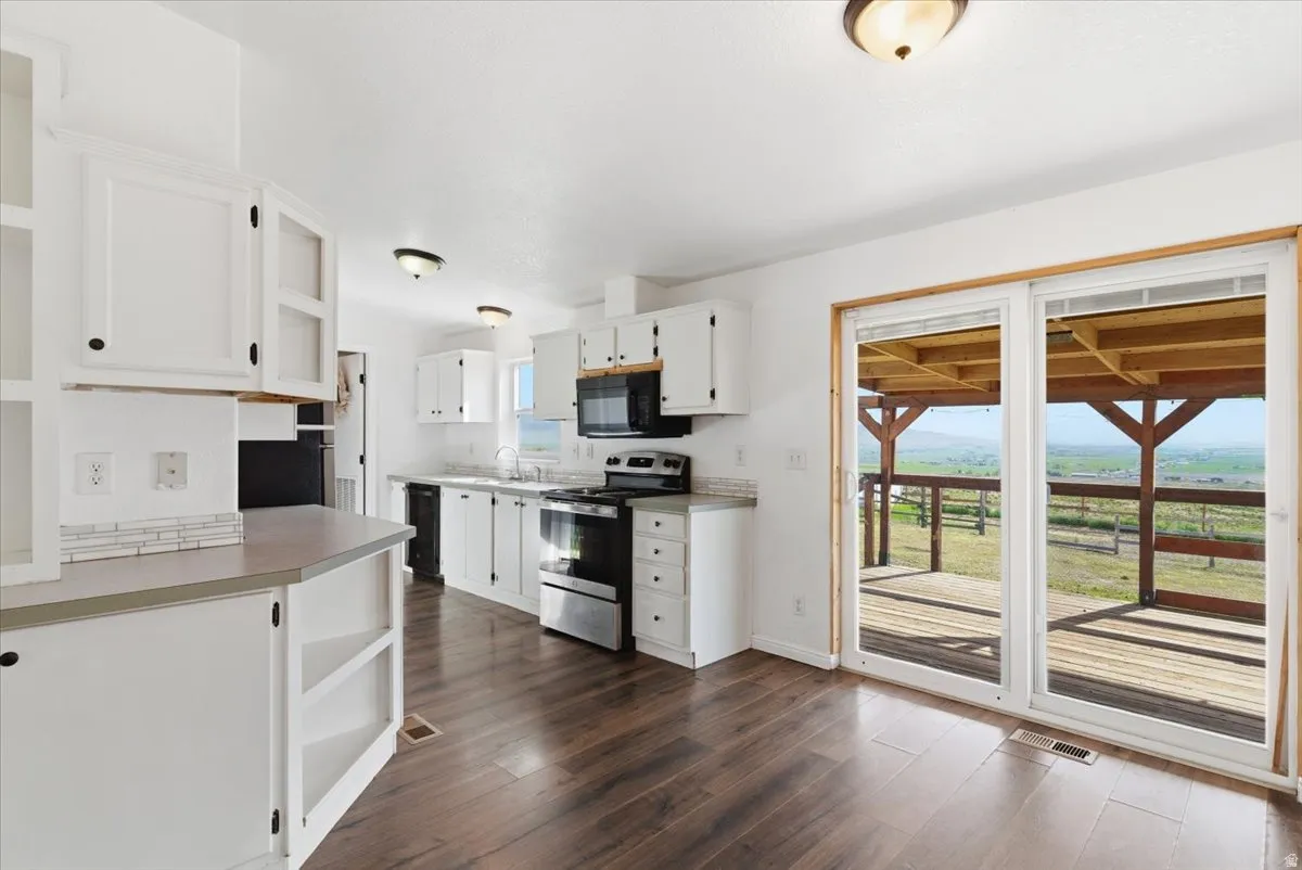 Kitchen featuring open shelves, black appliances, white cabinets, light countertops, and dark wood finished floors