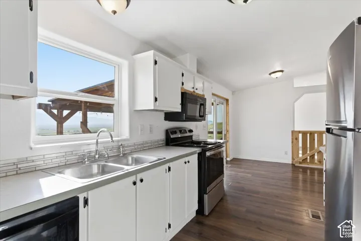 Kitchen with stainless steel appliances, light countertops, white cabinetry, and dark wood-style flooring