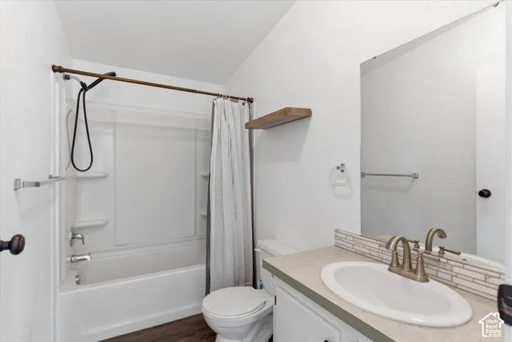Full bath featuring vanity, shower / bathtub combination with curtain, and dark wood finished floors