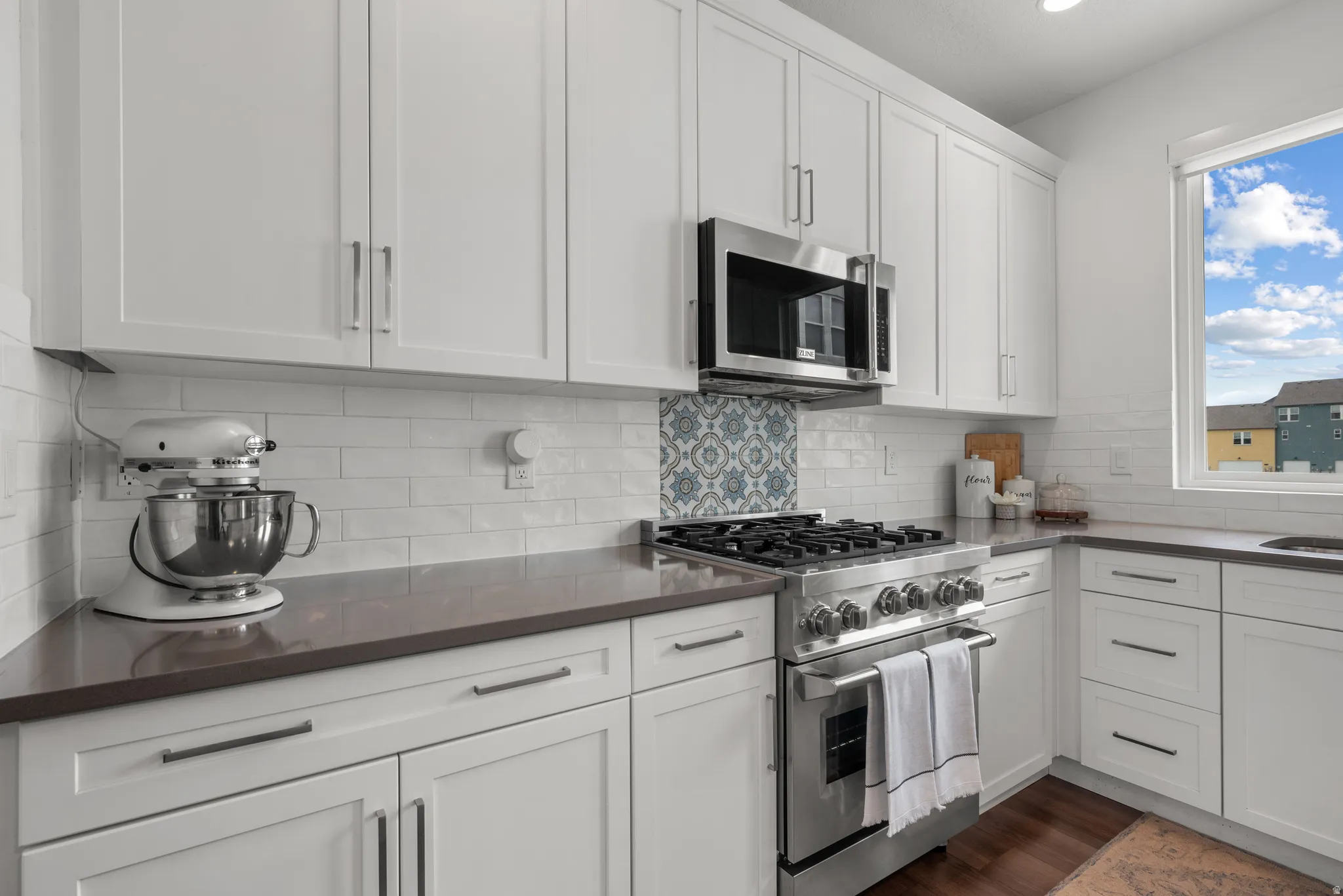 Kitchen with stainless steel appliances, white cabinets, dark wood-style floors, dark stone counters, and decorative backsplash