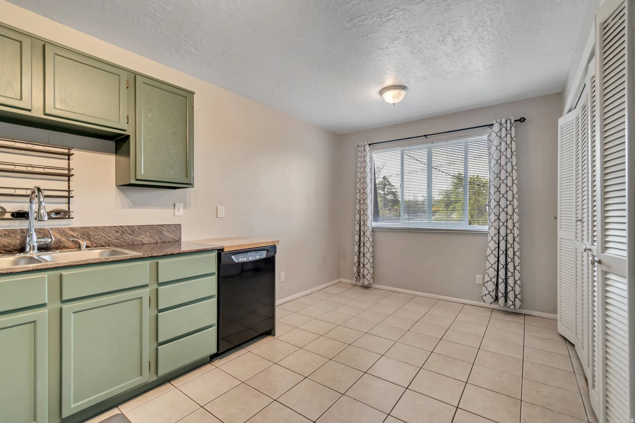 Kitchen with green cabinetry, a textured ceiling, dishwasher, and light tile patterned floors