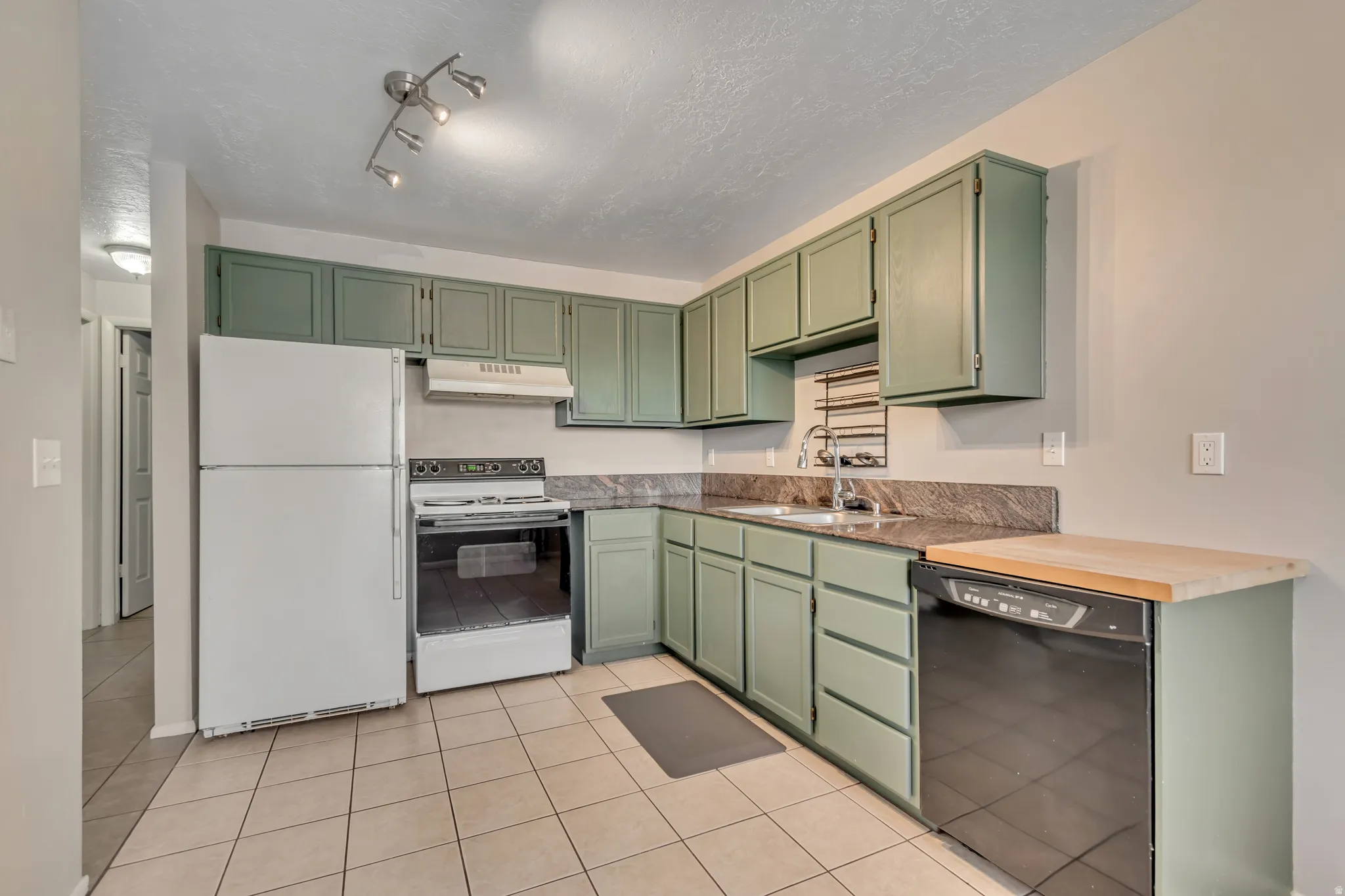 Kitchen with green cabinetry, white appliances, light tile patterned floors, rail lighting, and a textured ceiling
