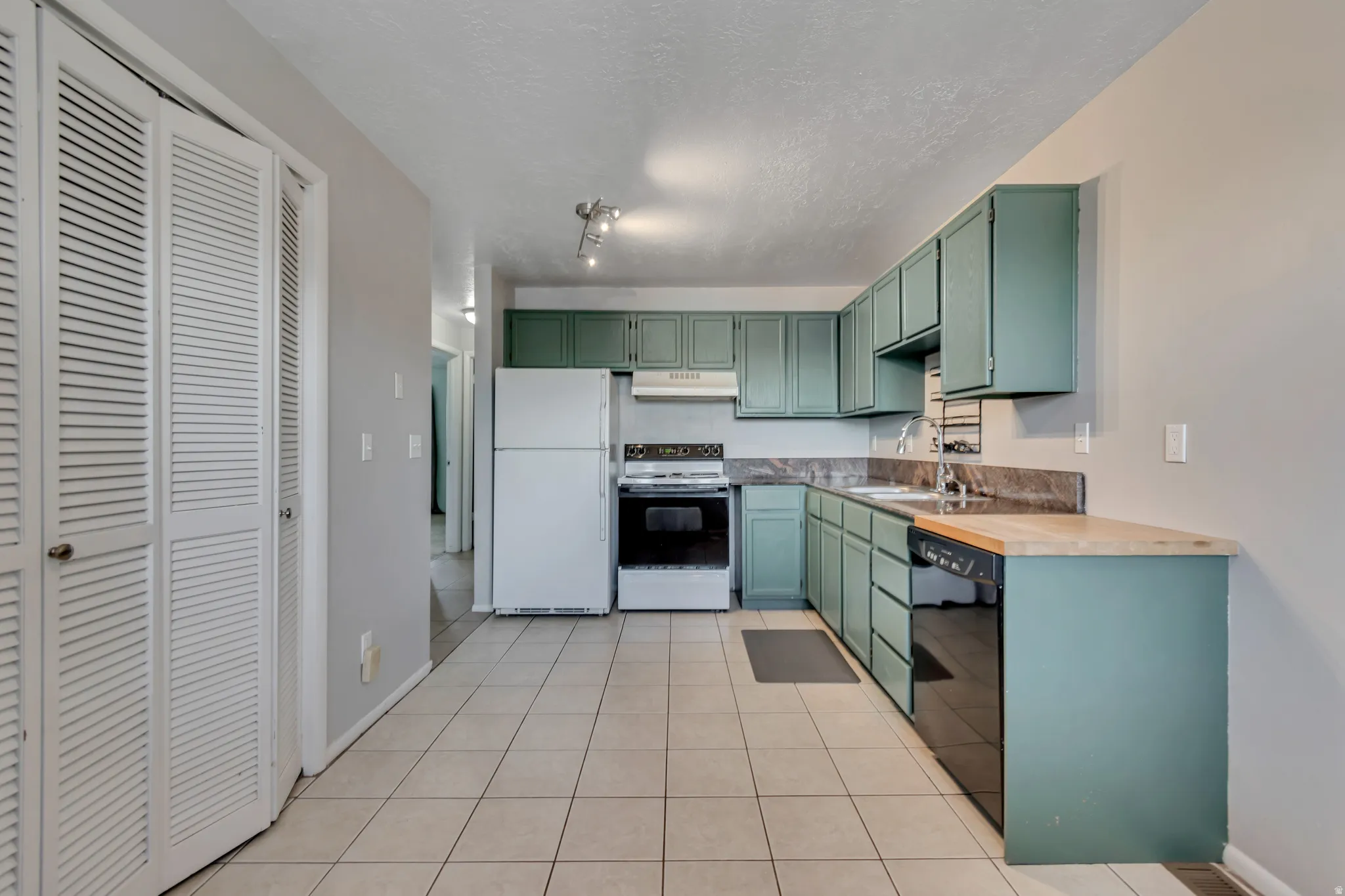 Kitchen featuring white appliances, green cabinets, light tile patterned flooring, a textured ceiling, and wooden counters