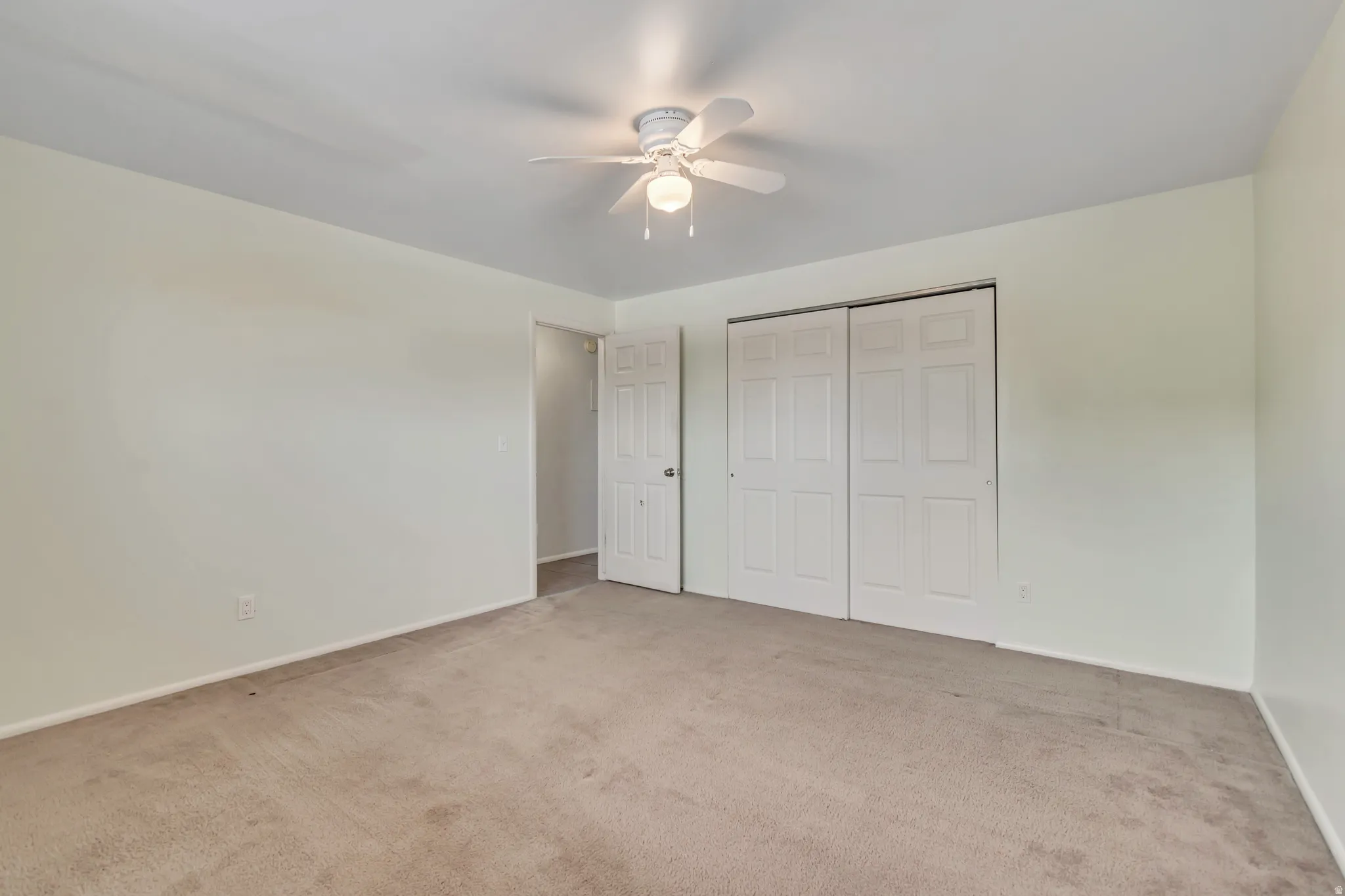 Unfurnished bedroom featuring light colored carpet, a closet, and a ceiling fan