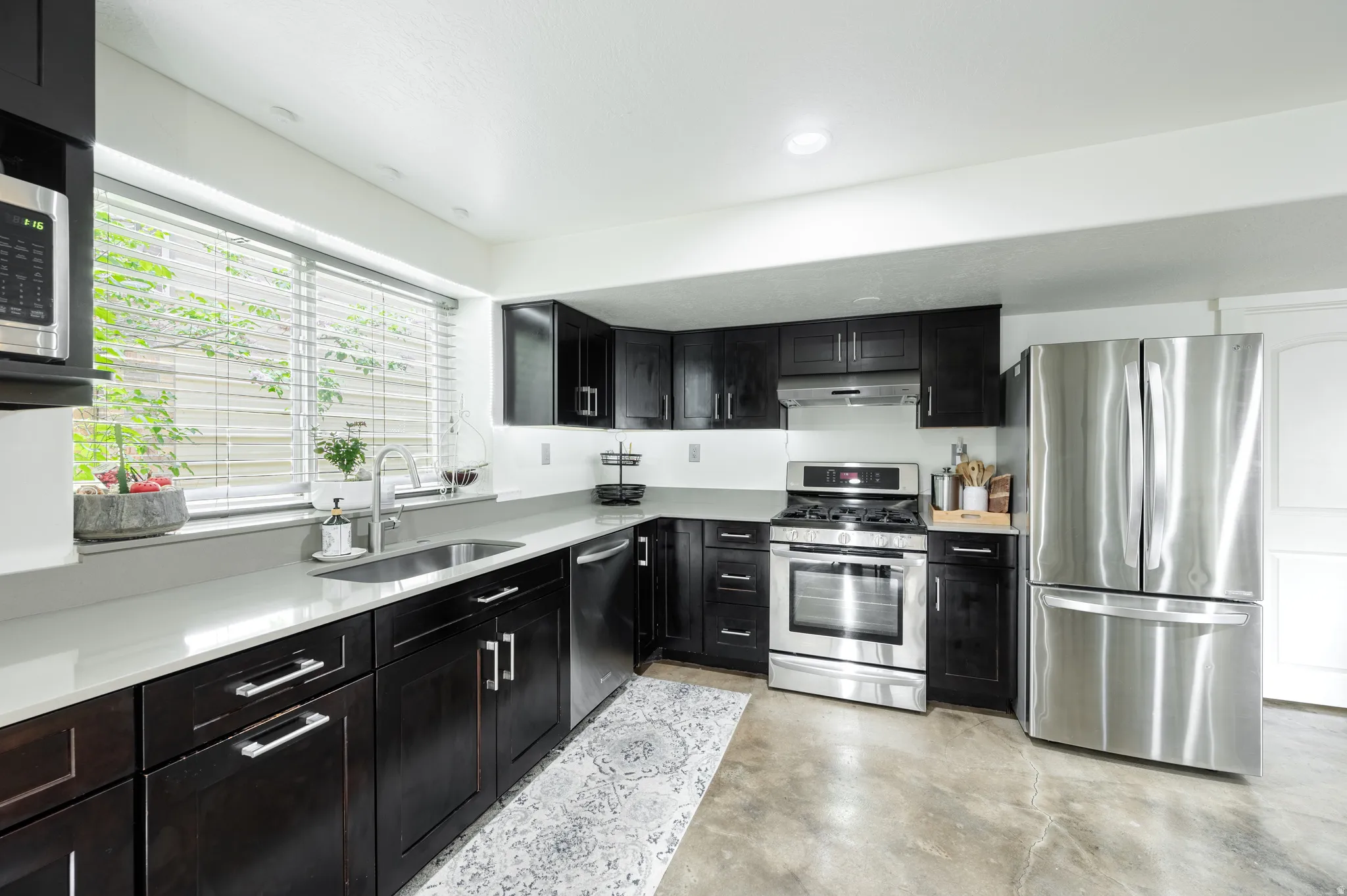 Kitchen with stainless steel appliances, concrete floors, dark cabinetry, light stone countertops, and recessed lighting