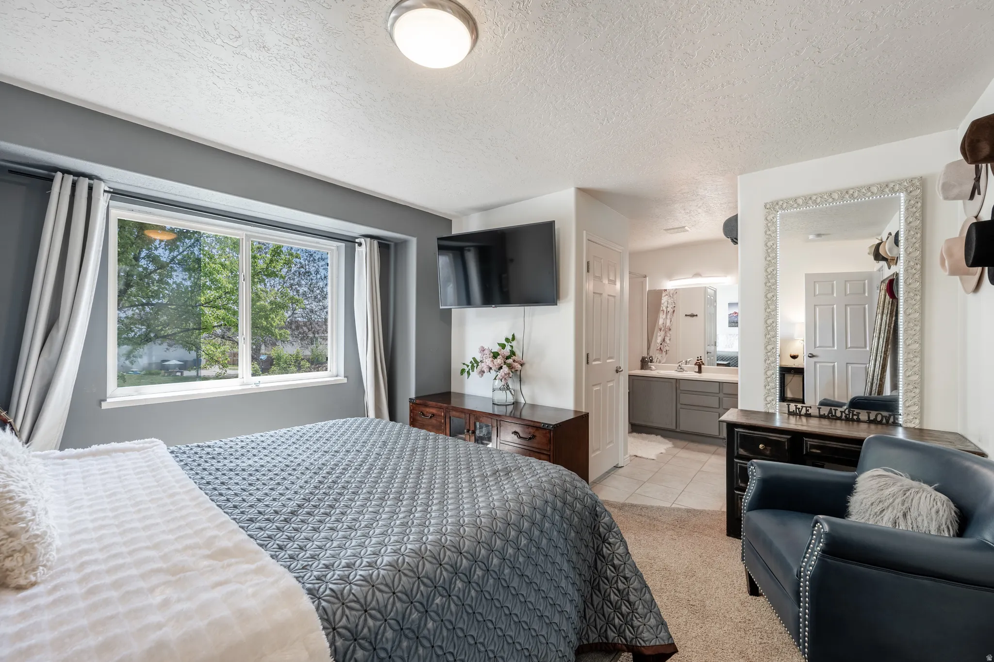 Bedroom featuring a textured ceiling, light carpet, ensuite bath, and light tile patterned floors