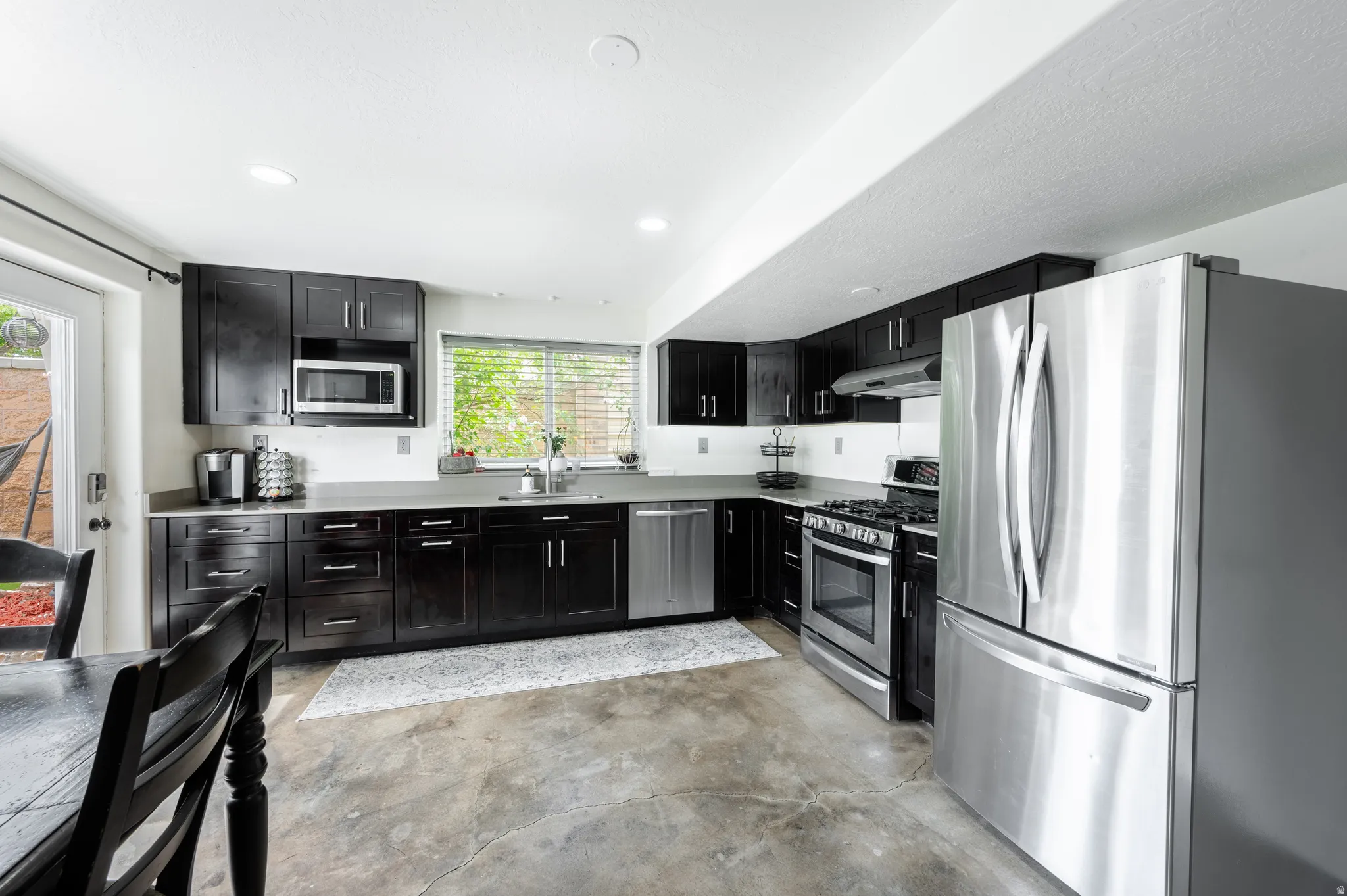 Kitchen with stainless steel appliances, dark cabinets, recessed lighting, light countertops, and concrete floors
