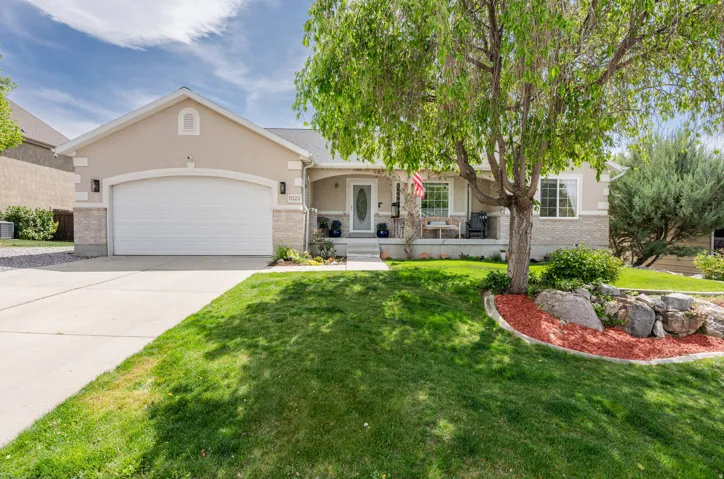 View of front of home with covered porch, a garage, driveway, stucco siding, and a front lawn
