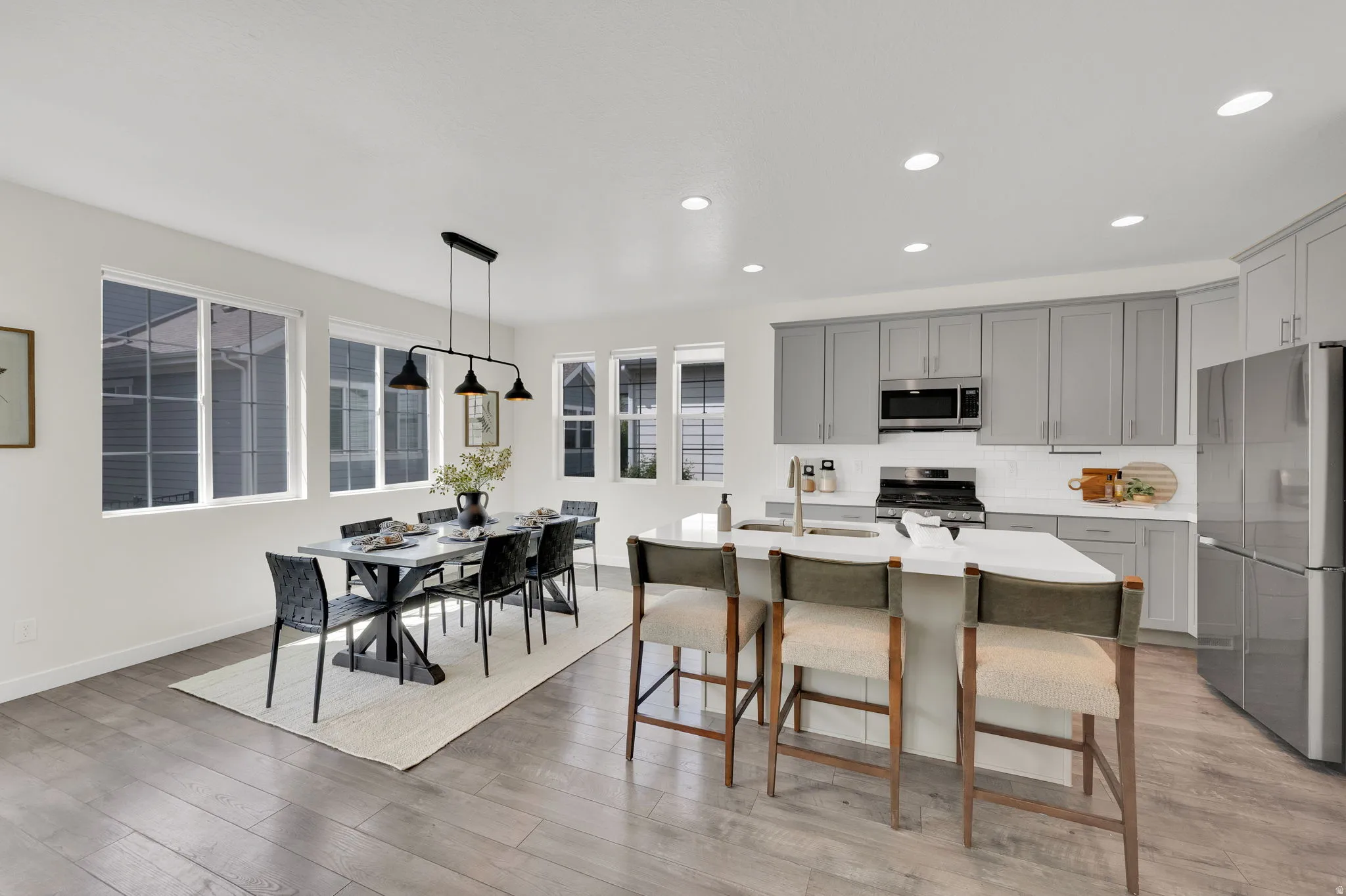 Kitchen featuring stainless steel appliances, gray cabinets, a kitchen breakfast bar, tasteful backsplash, and pendant lighting